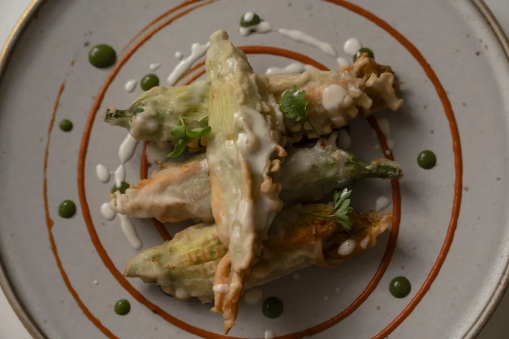 Fiori di zucca in pastella fritti su piatto bianco con salsa verde e piselli