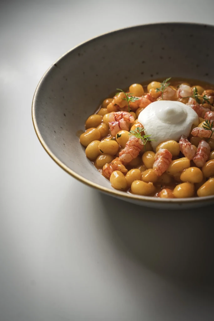 Ciotola di ceci in umido con salsa di pomodoro, guarniti con una quenelle di yogurt e erbe fresche