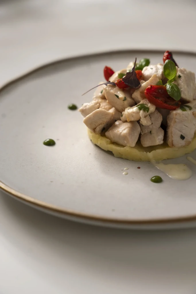 Tartare di pesce bianco con pomodorini rossi e crema verde su piatto bianco in stile gastronomico