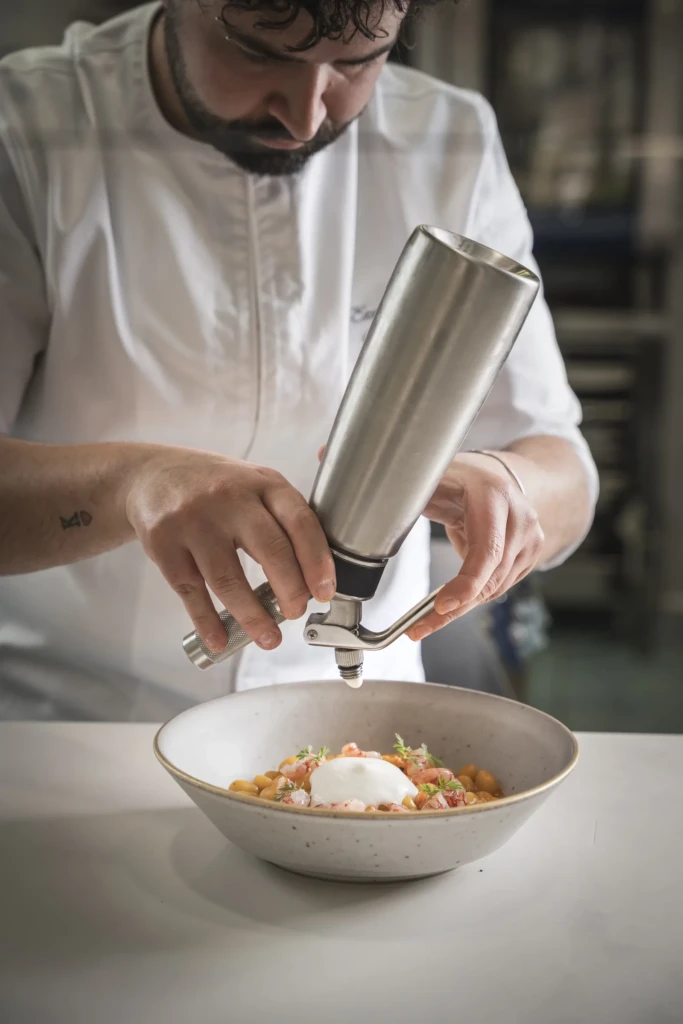Chef con grembiule bianco macina pepe su un piatto di pasta con pomodoro e burrata in un ristorante